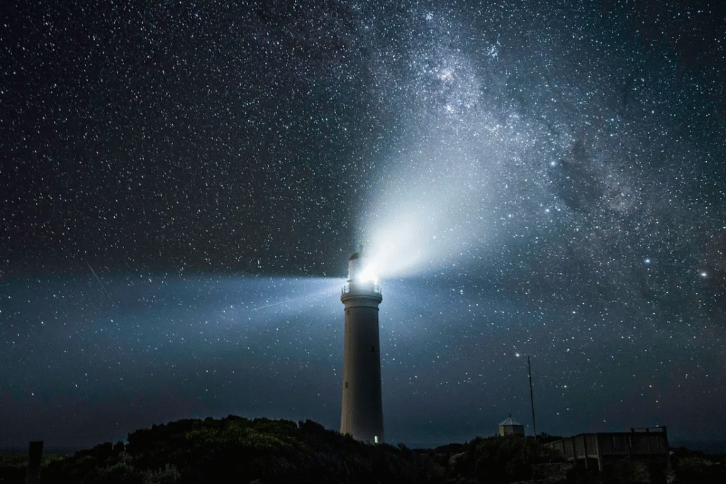 A lighthouse shining its beam across a dark, star-filled night sky, creating an eerie coastal scene that fits the Flannan Isles Lighthouse mystery.